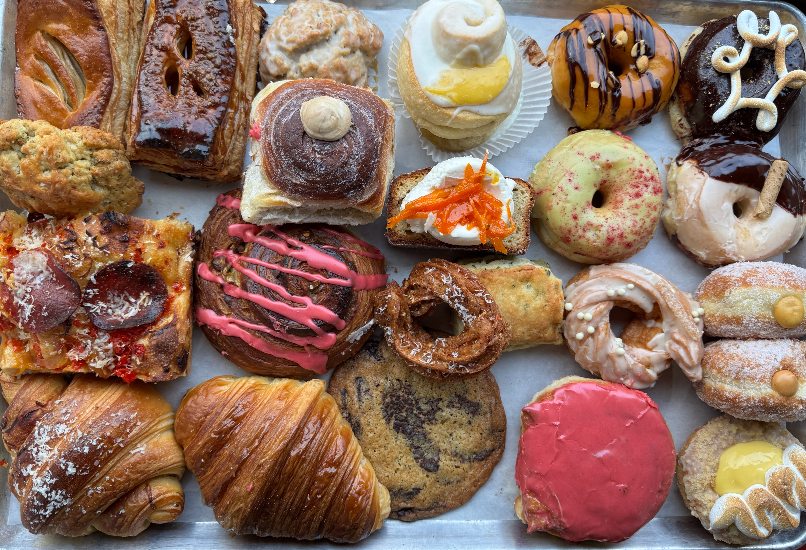 An assortment of Black Magic Bakehouse croissants, doughnuts, scones, and savory pastries on baking trays